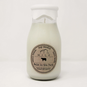 A white soy candle with a clear label that reads 'Milk' and 'Walk in the Park,' along with the brand 'L.A.