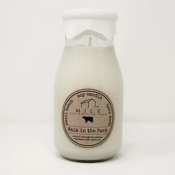 A white soy candle with a clear label that reads 'Milk' and 'Walk in the Park,' along with the brand 'L.A.