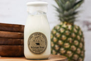 Milk bottle with a label on a wooden surface next to a pineapple