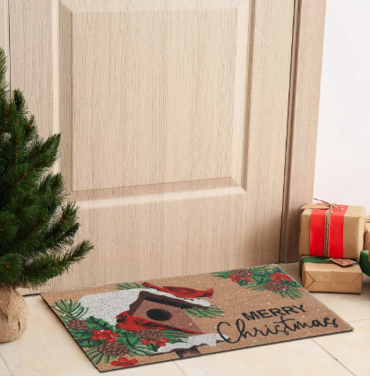 Christmas-themed doormat with a birdhouse design and 'Merry Christmas' text, placed on a wooden floor in front of a door.