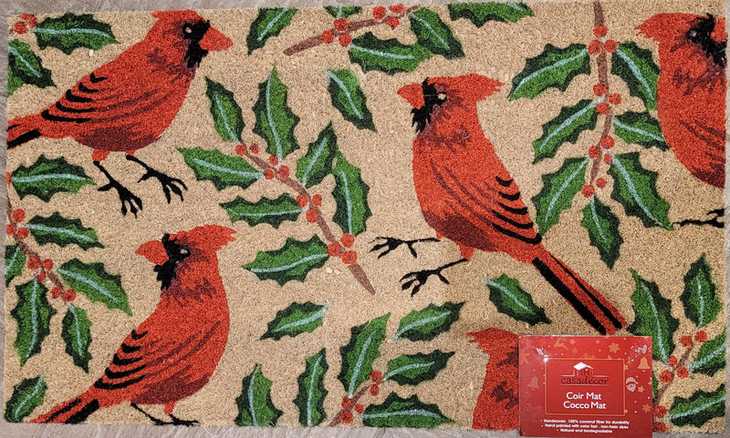 Doormat with red cardinals and holly design, featuring a small box of cocoa mix.