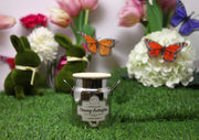 Candle with 'Chasing Butterflies' label on grass with decorative elements like flowers, butterflies, and a rabbit.
