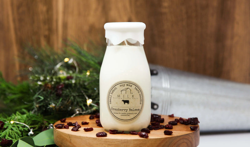 Milk bottle labeled 'Cranberry Balsam' on a wooden board with decorative elements.