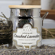Candle in a metal container with a wooden lid, featuring a label for 'Crushed Lavender' candle.