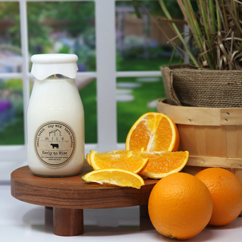 Milk bottle labeled 'Early to Rise' with sliced oranges on a wooden stand outdoors.