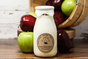 White bottle labeled 'Farm Stand Apple' with apples in the background on a wooden surface.