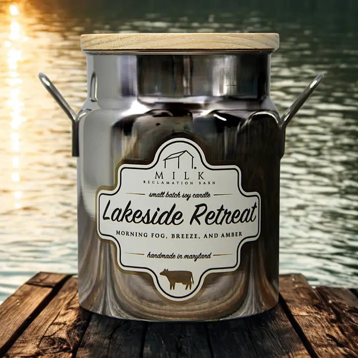 Candle jar labeled 'Lakeside Retreat' by Milk Reclamation Barn on a wooden surface with a water background.