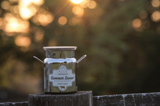 Candle labeled 'Summer Sunset' on a wooden surface with a blurred natural background