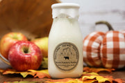 Bottle of Apple Pumpkin Butter with a label, surrounded by apples and a pumpkin, on a wooden surface.