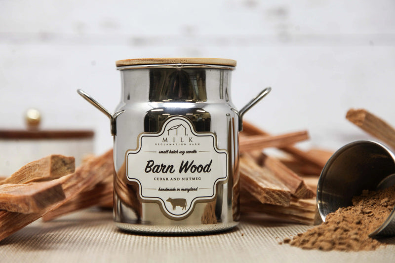 Candle jar labeled 'Barn Wood' with cinnamon sticks and a scoop of spice on a textured surface.