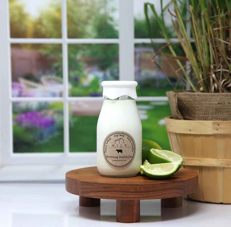 White bottle with a label on a wooden stand in front of a window with a garden view