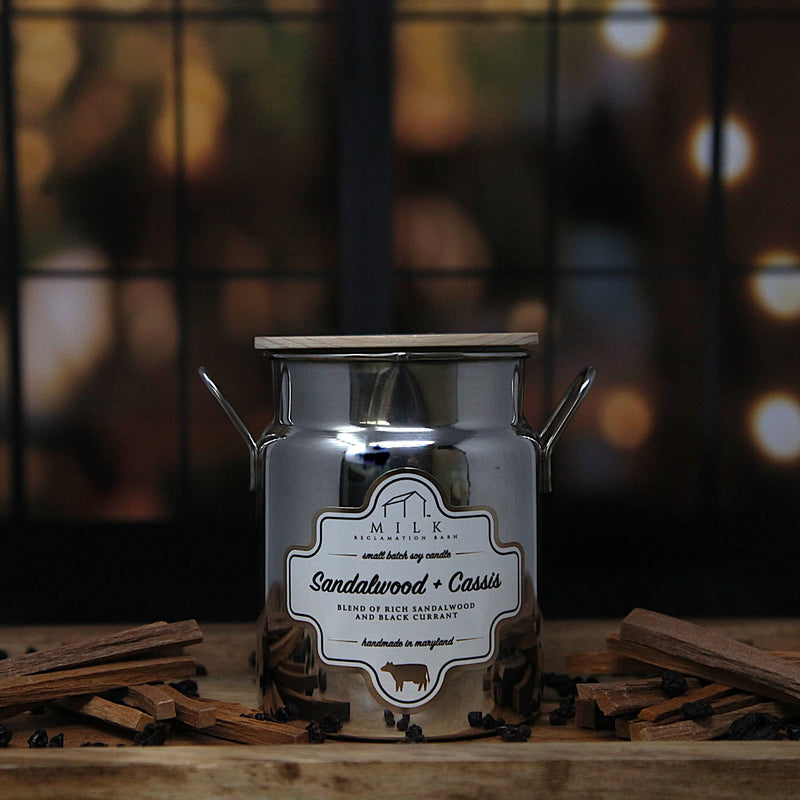 Candle jar labeled 'Sandalwood + Cassis' with a blurred background