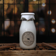 Milk bottle-shaped candle with a label on a wooden surface with cinnamon sticks.