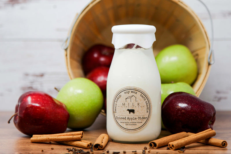 Milk bottle labeled 'Spiced Apple Cider' with apples and cinnamon sticks on a wooden surface.