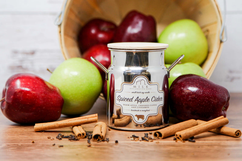 Jar of 'Spiced Apple Cider' candle with apples and cinnamon sticks on a wooden surface
