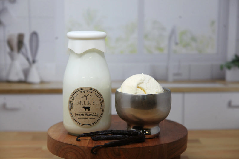 Bottle of vanilla ice cream with a label next to a bowl of ice cream on a wooden surface.