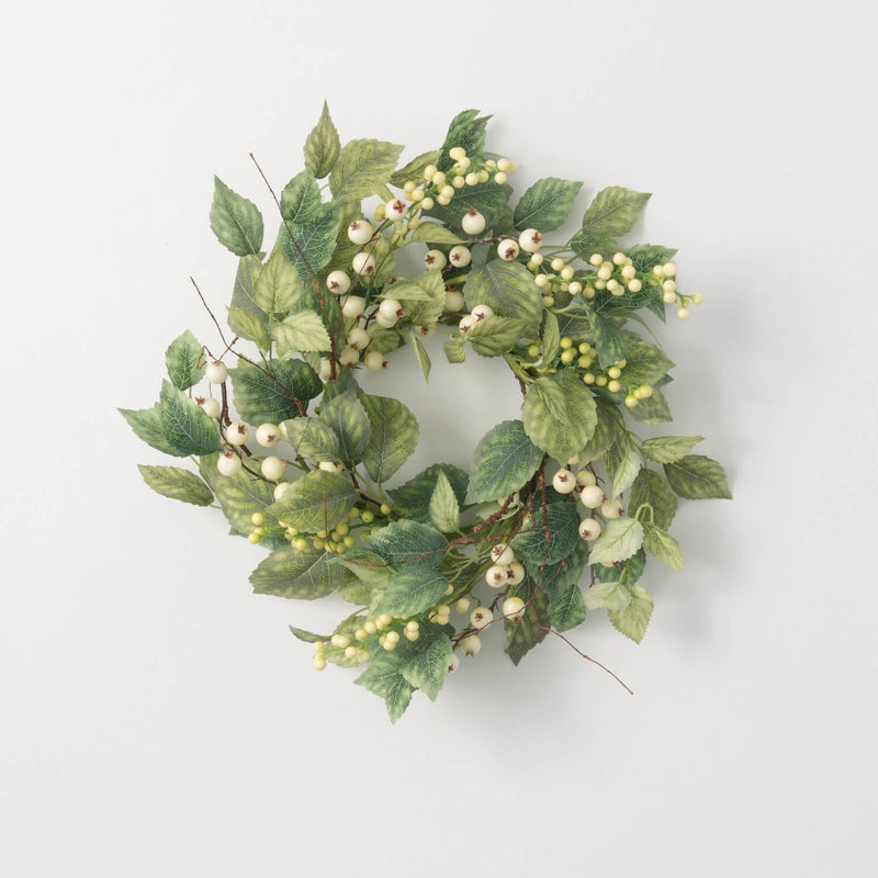 Green leafy wreath with small white berries on a light gray background