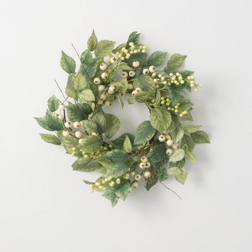 Green leafy wreath with small white berries on a light gray background