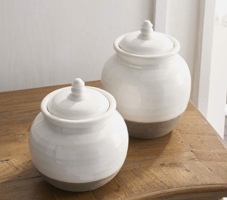 Two white ceramic jars with brown bases on a wooden surface.