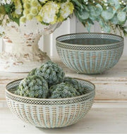 Decorative woven bowls with green decorative balls and flowers on a light wooden surface.