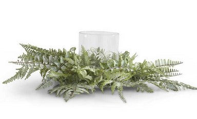 Decorative arrangement with green foliage and a clear candle holder on a white background