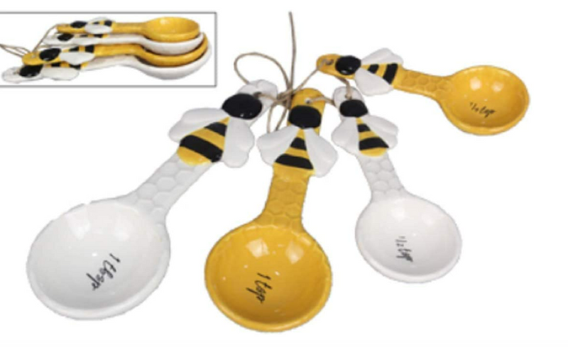 Set of four ceramic measuring spoons with bee design on a white background