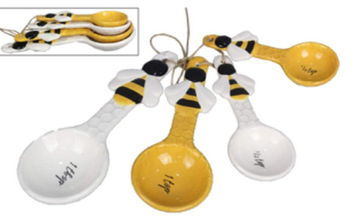 Set of four ceramic measuring spoons with bee design on a white background