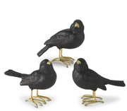Three black bird figurines with gold feet on a white background