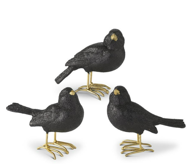 Three black bird figurines with gold feet on a white background