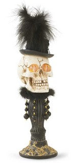 Decorative skull with top hat, feathers, and ornate stand on a white background