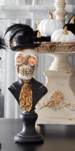 Decorative skull bust with a top hat and orange eyes on a black stand, with white pumpkins in the background.