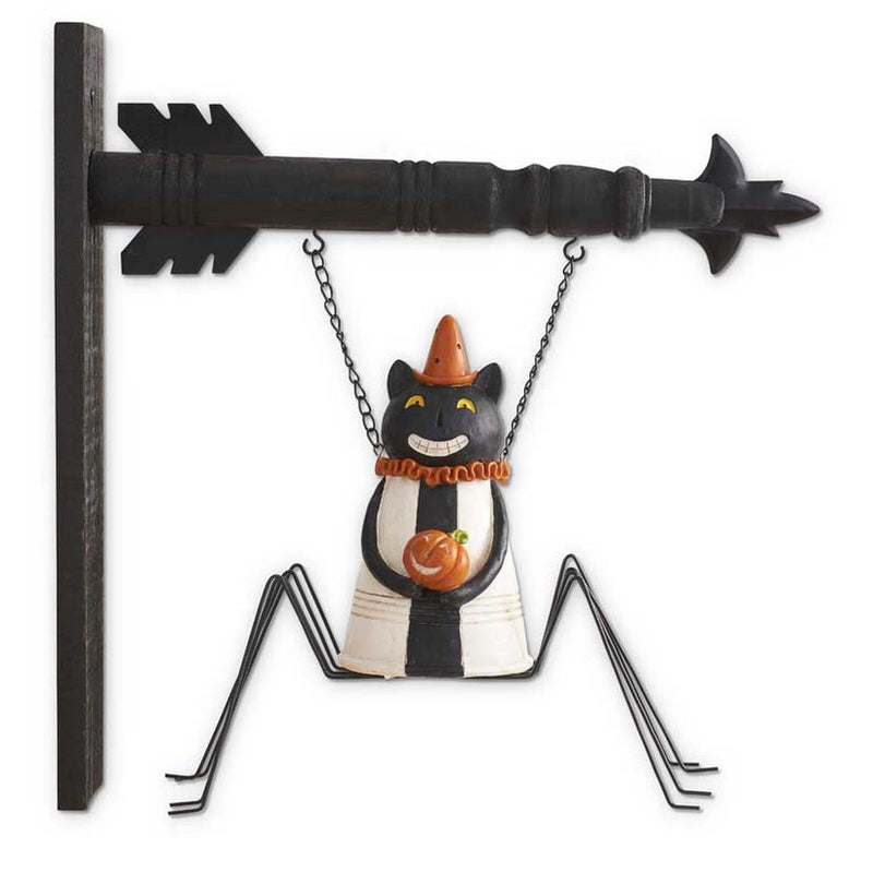 Decorative cat figurine with a cone hat hanging from a black metal arrow on a white background