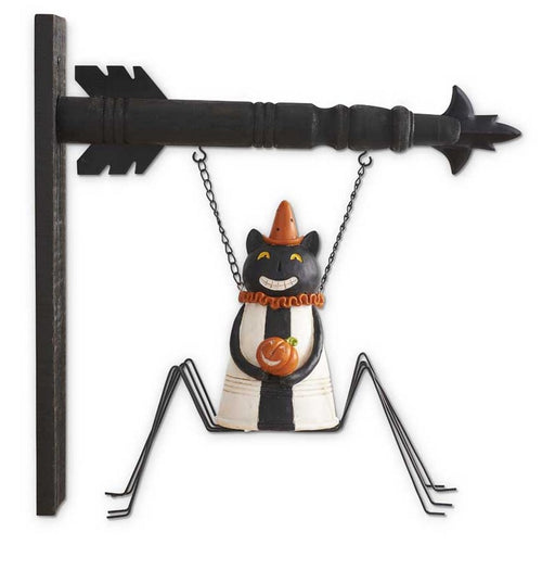 Decorative cat figurine with a cone hat hanging from a black metal arrow on a white background