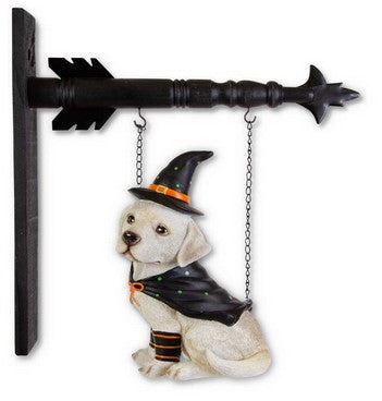 Dog figurine in a witch costume hanging on a decorative arrow with chains.