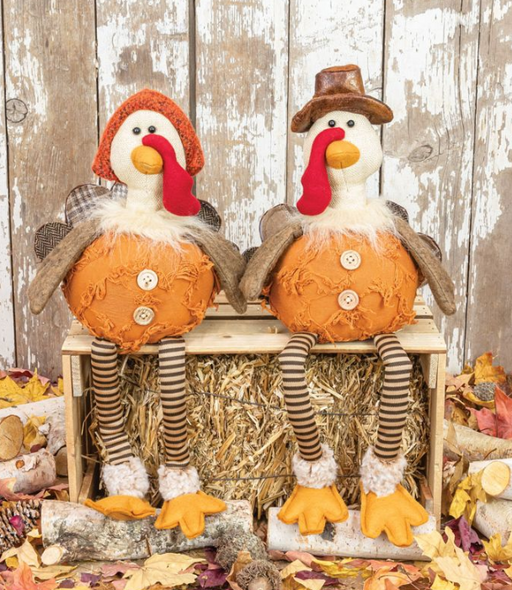 Two decorative turkeys on pumpkins with fall leaves and hay in the background