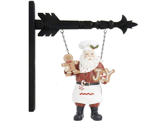 Decorative wall hanging with Santa Claus holding a 'Joy' sign and gingerbread man, attached to a black arrow-shaped stand.