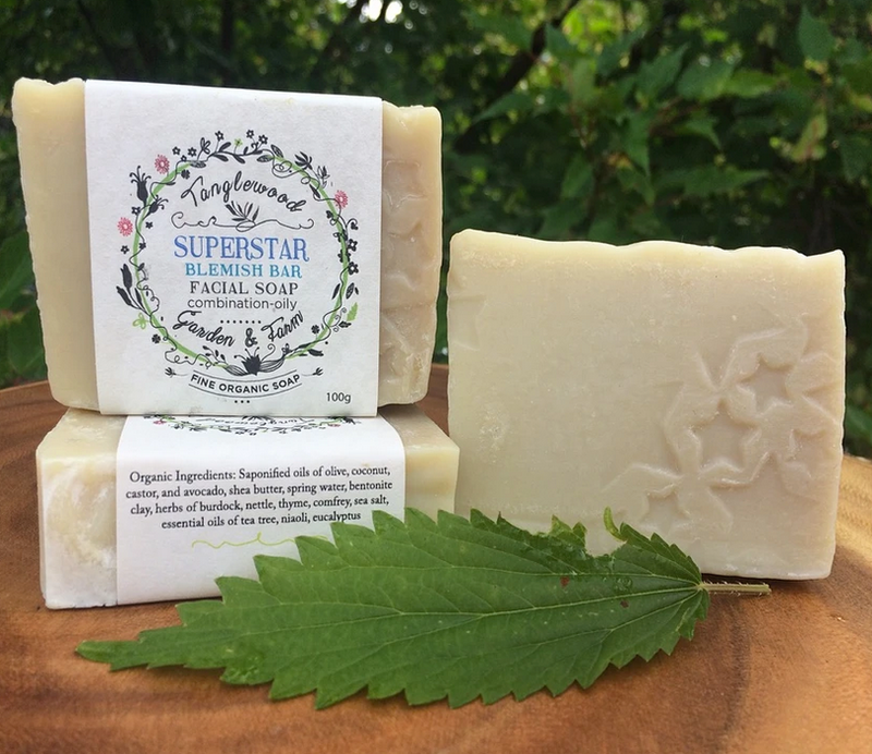 Two bars of facial soap with labels on a wooden surface with greenery in the background