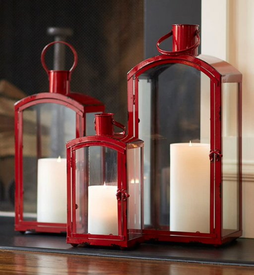 Three red lanterns with white candles inside on a reflective surface.