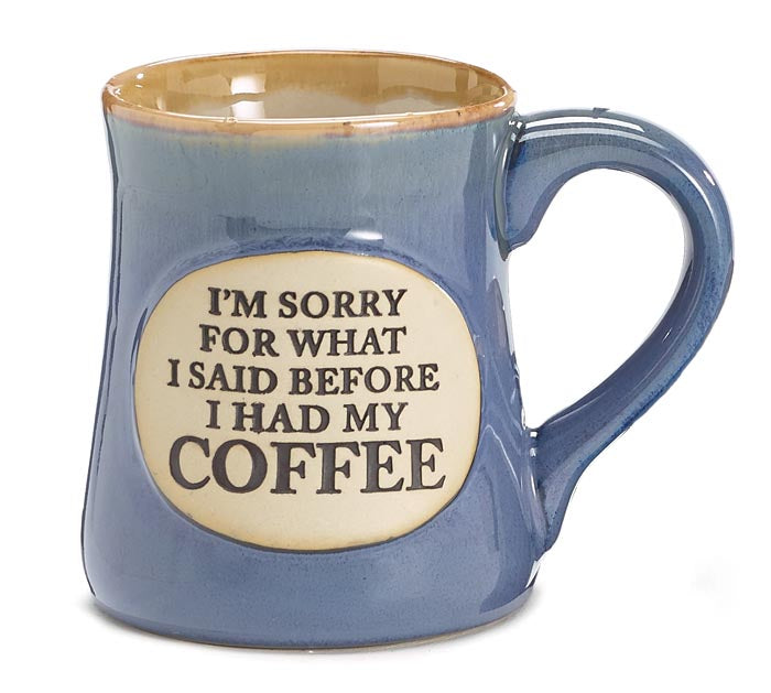 A blue porcelain mug with a tan rim and an oval medallion that reads 'I'm sorry for what I said before I had my coffee'.