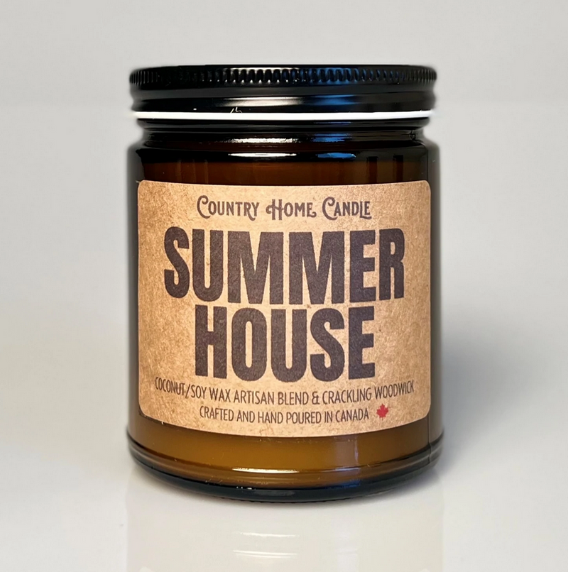 A white jar candle with a black lid, labeled 'Summer House - Country Home Candle' with blue and green text.