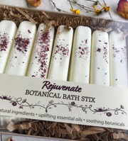 A package of white rectangular botanical bath stix with various botanicals sprinkled on top, displayed in a box.