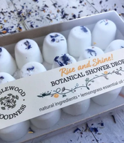 Packaging of Botanical Shower Drops with 'Rise and Shine' lemongrass scent labeled, displaying the product as white spherical drops with floral patterns.