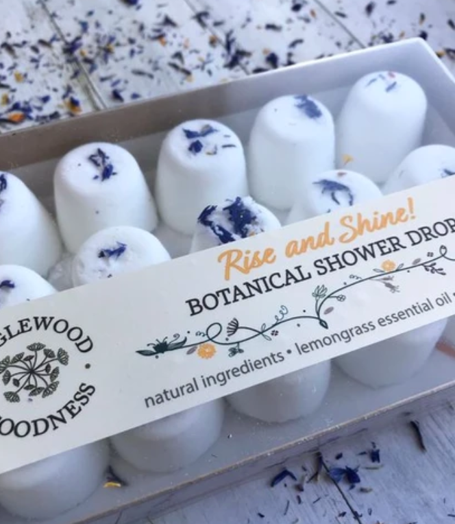 Packaging of Botanical Shower Drops with 'Rise and Shine' lemongrass scent labeled, displaying the product as white spherical drops with floral patterns.
