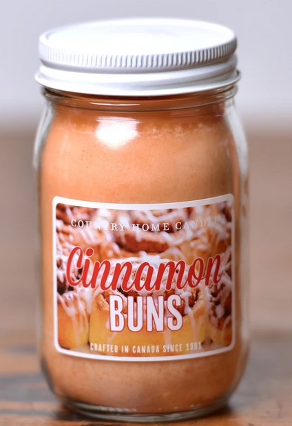 Jar of cinnamon bun-flavored candle with a label on a wooden surface