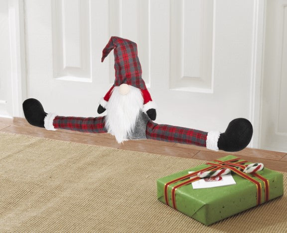 Decorative gnome in plaid pants and hat next to a green gift box on a wooden floor.