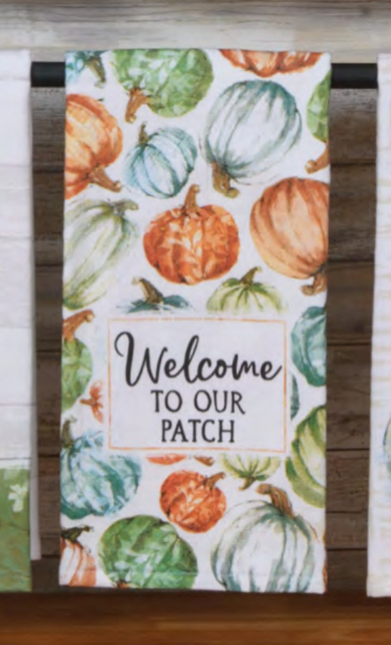 Decorative towel with pumpkins and gourds design and 'Welcome to our patch' text on a wooden background.