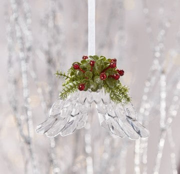 Decorative hanging angel ornament with greenery and red berries against a sparkling silver background