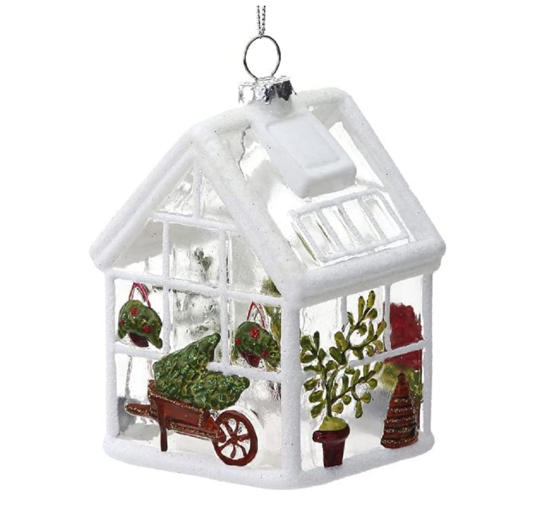 Decorative glass greenhouse ornament with plants and a wheelbarrow on a white background